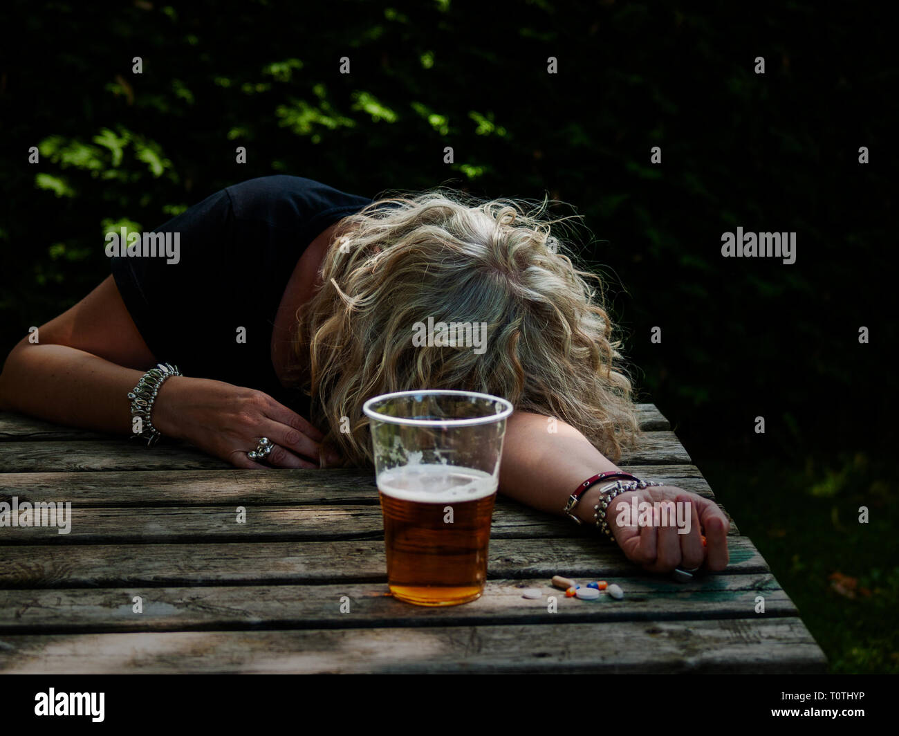 Una donna con un gran numero di pillole in mano di diversi colori e dimensioni e un bicchiere di birra a un tavolo per esterno Foto Stock