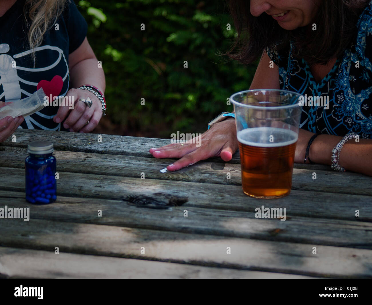 Due donne preparano una linea di cocaina su un tavolo di legno con un bicchiere di birra sul lato Foto Stock