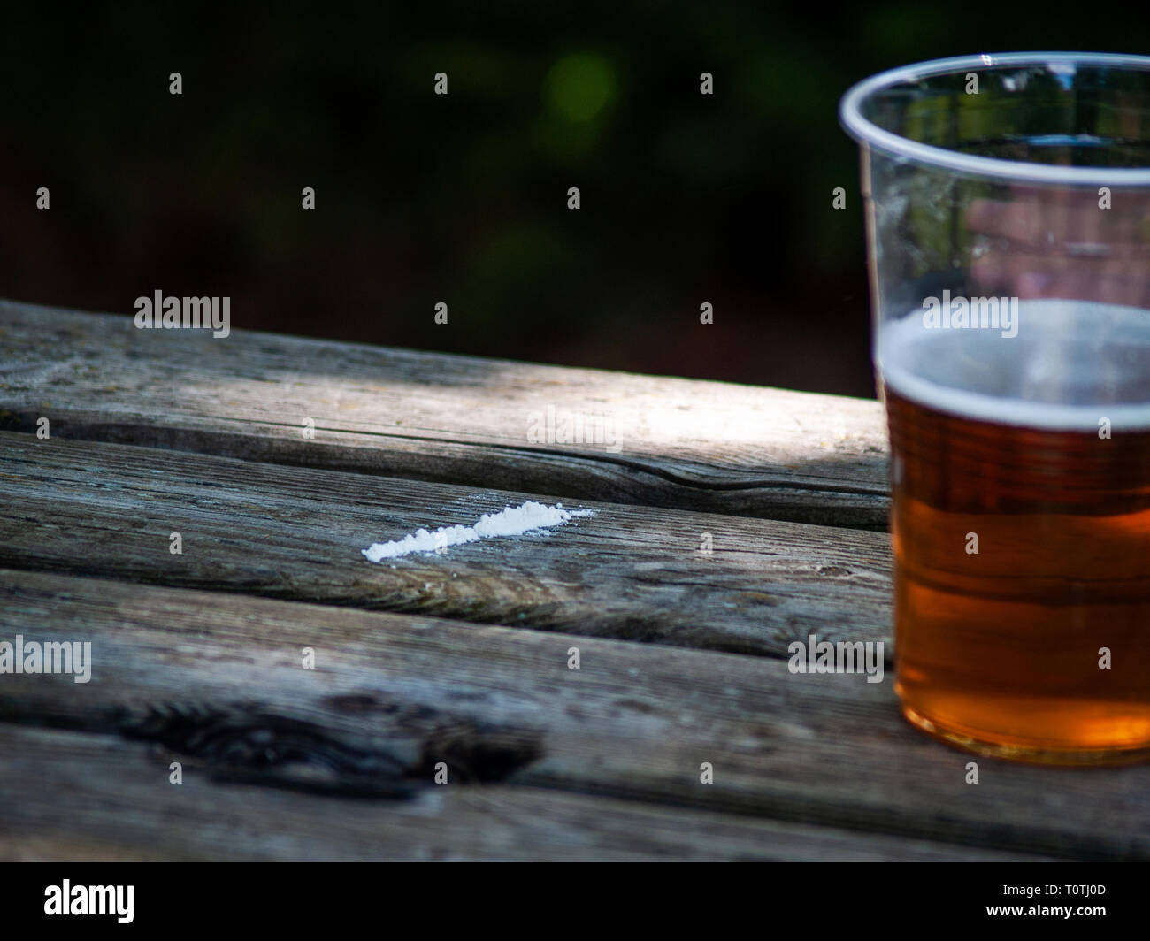 Una linea di cocaina su un tavolo di legno con un bicchiere di birra sul lato Foto Stock