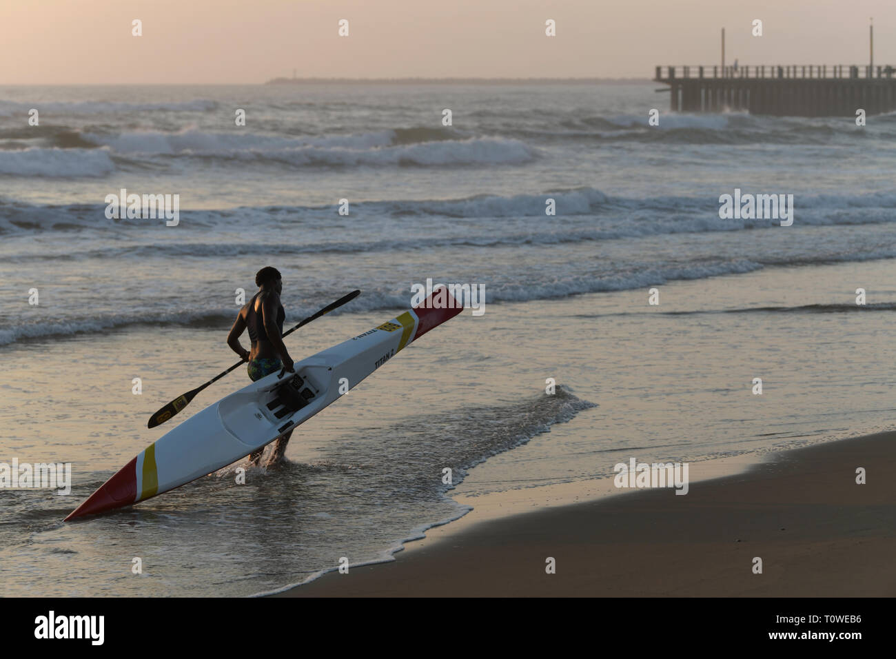 Durban, KwaZulu-Natal, Sud Africa, singolo adulto uomo a camminare con paddle ski Canoe sulla spiaggia, persone, paesaggio Foto Stock