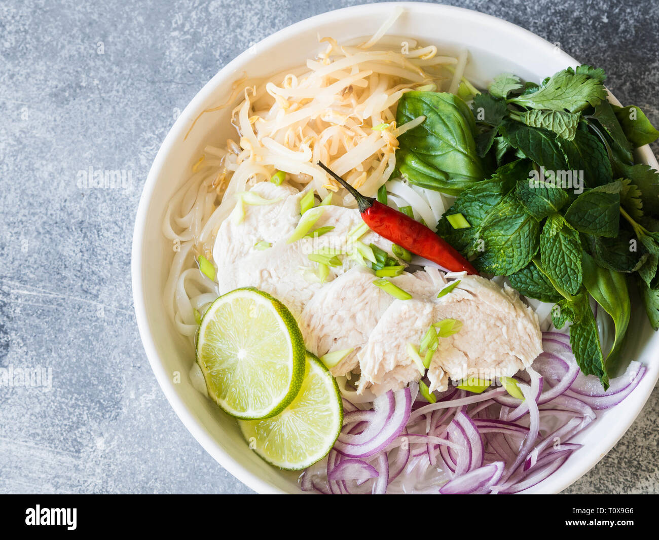Tradizionale zuppa vietnamita- pho ga in bianco ciotola con pollo e riso tagliatelle, menta e coriandolo, verde e rosso cipolla, peperoncino, i germogli di soia e calce Foto Stock