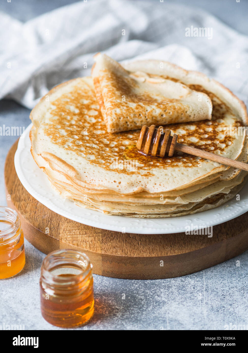 Pila russo in casa il lievito Pancake sulla piastra bianca, legno cucchiaio di miele e il miele in vasetti sul tavolo. Tradizionale frittelle di frumento per Shrovetide. Foto Stock