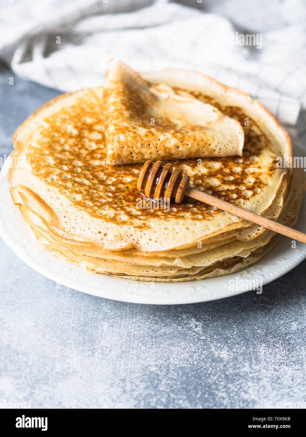 Pila russo in casa il lievito Pancake sulla piastra bianca, legno cucchiaio di miele sul tavolo. Tradizionale crepes di grano per Shrovetide. Foto Stock