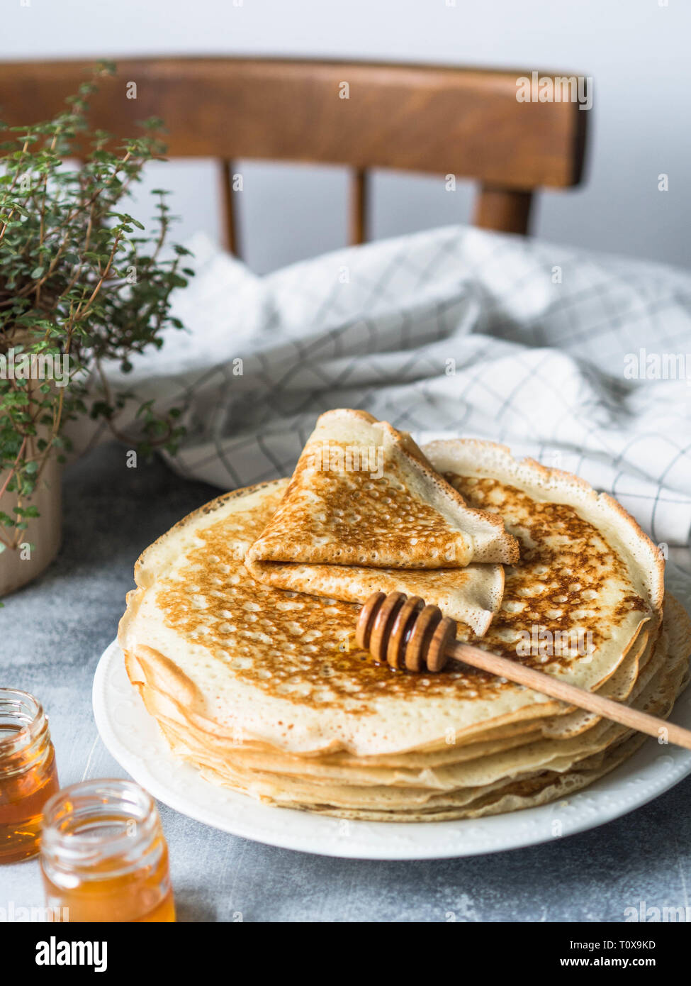 Pila russo in casa il lievito Pancake sulla piastra bianca, legno cucchiaio di miele e il miele in vasetti sulla tabella grigia. Tradizionale frittelle di frumento per Shrovetide. Foto Stock