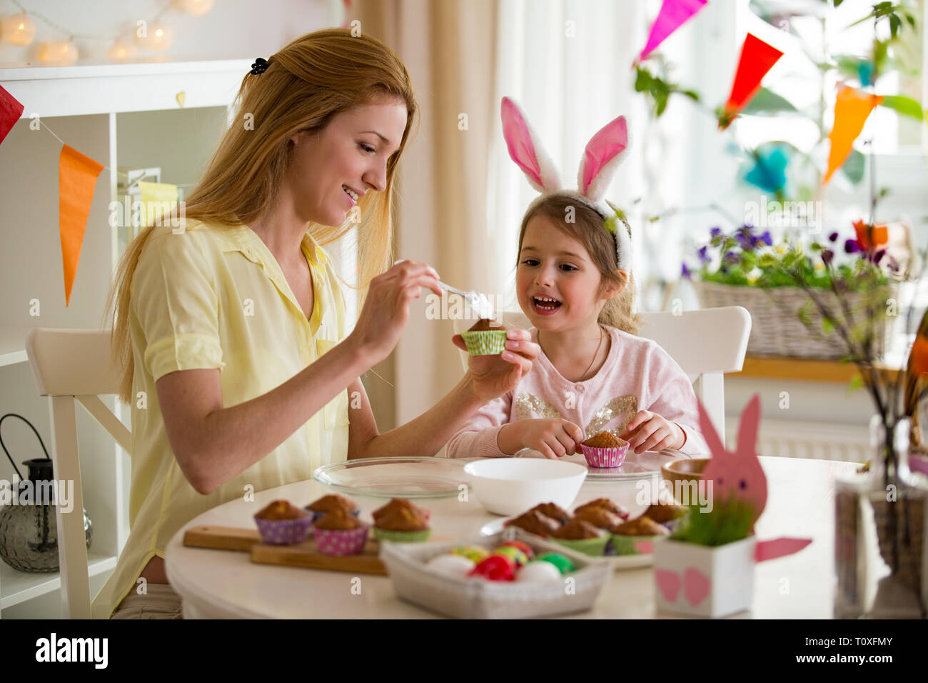 Madre e figlia che celebrano la Pasqua, tortini di cottura, copertura con smalto. La famiglia felice vacanza. Carino bambina nelle orecchie di coniglietto. Foto Stock