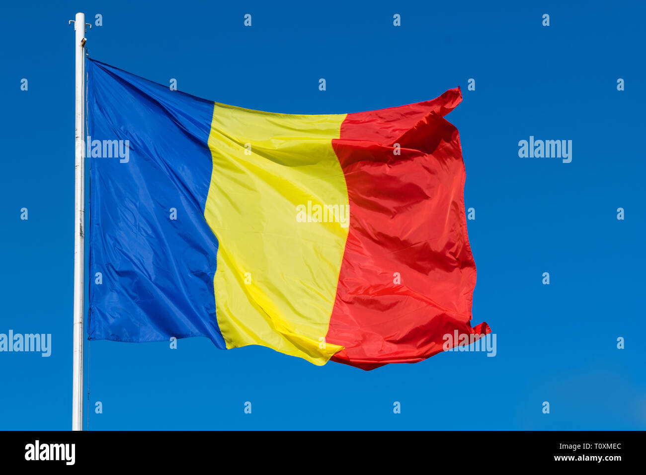 Bandiera della Romania sul post che si muovono nel vento. Il rumeno rosso e verde e la Bandiera blu sventola nel vento con chiaro sfondo blu. Foto Stock
