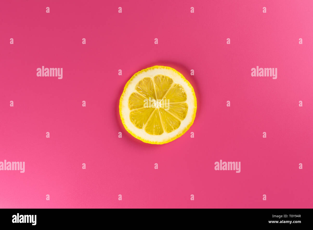 Una singola fetta di limone isolata su uno sfondo rosa, illuminati da una luce tenue. Foto Stock