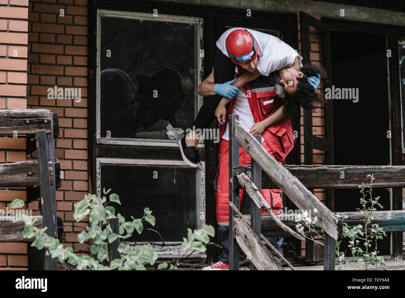 Lavoratore di salvataggio che porta la donna fuori di casa danneggiata. Foto Stock