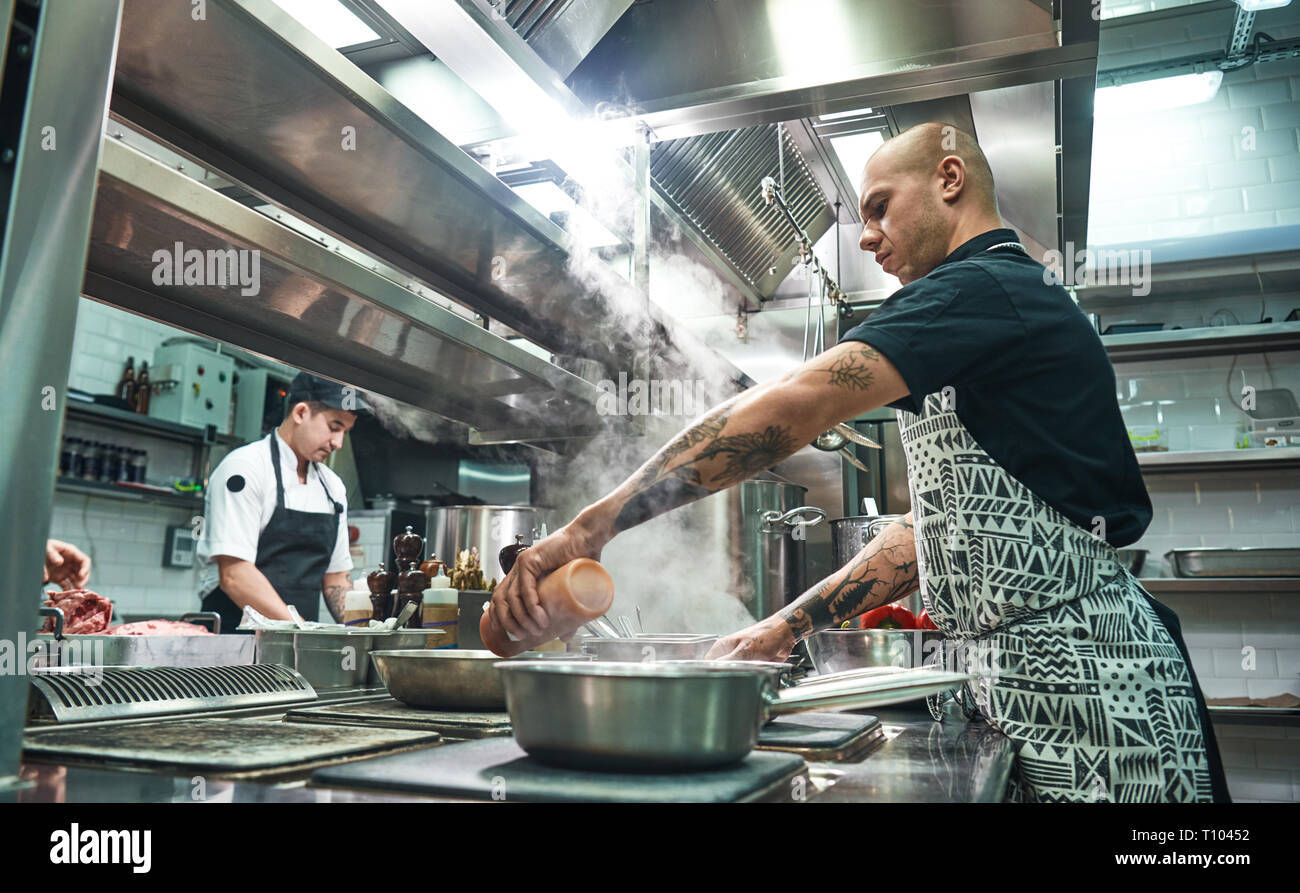 Come cuocere un concentrato di carne giovane chef di grembiule e cuoce preparare il cibo insieme in un ristorante di cucina. Il processo di cottura Foto Stock