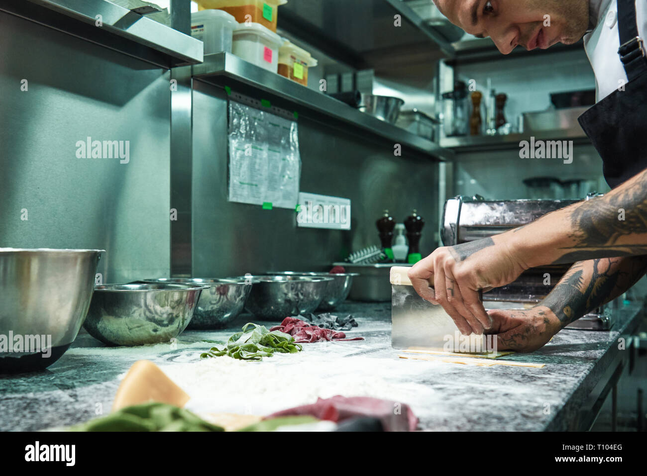 La perfezione. Serietà professionale chef con tatuaggi sulle mani di pasta da taglio sul tavolo di cucina con farina per pasta italiana. Il processo di cottura Foto Stock