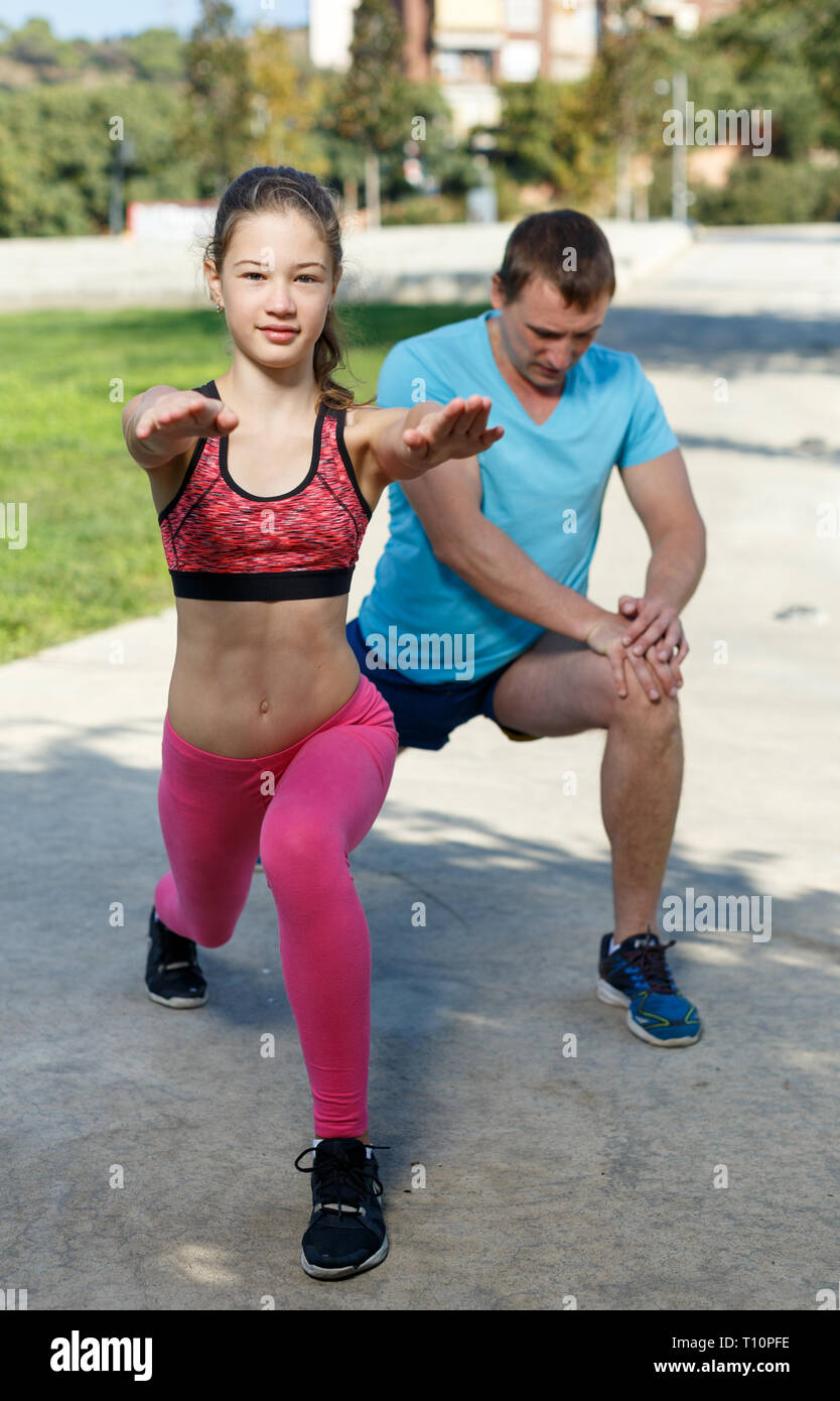 Felice di tween girl stretching insieme con padre durante il corso di formazione all'aperto nel giorno di estate Foto Stock