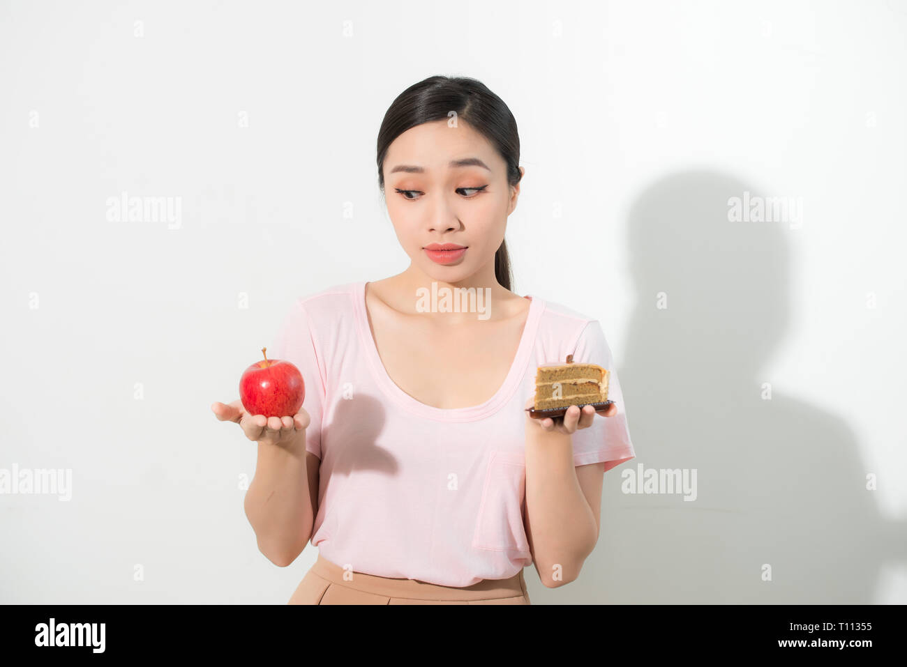 La donna tiene in mano la torta dolce e frutta apple scegliendo, cercando di resistere alla tentazione di fare la giusta scelta della dieta. Perdita di peso la dieta dilemma golosità Foto Stock