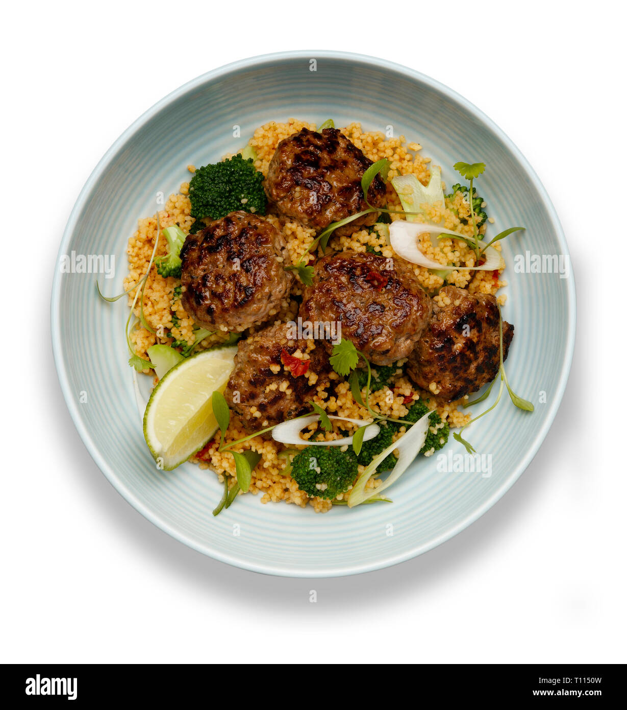 Una ciotola di succulente Harissa polpettine di carne su un letto di cuscus isolato su bianco con ombra Foto Stock