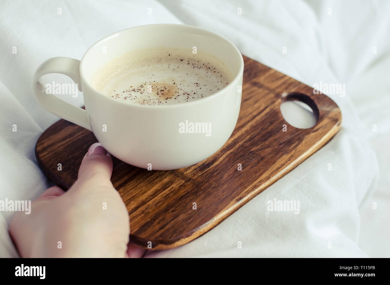 Una tazza di caffè in mano femminile nel letto su una coltre bianca. Moman godendo del comfort a casa accogliente atmosfera. Buona mattina. POV. Foto Stock