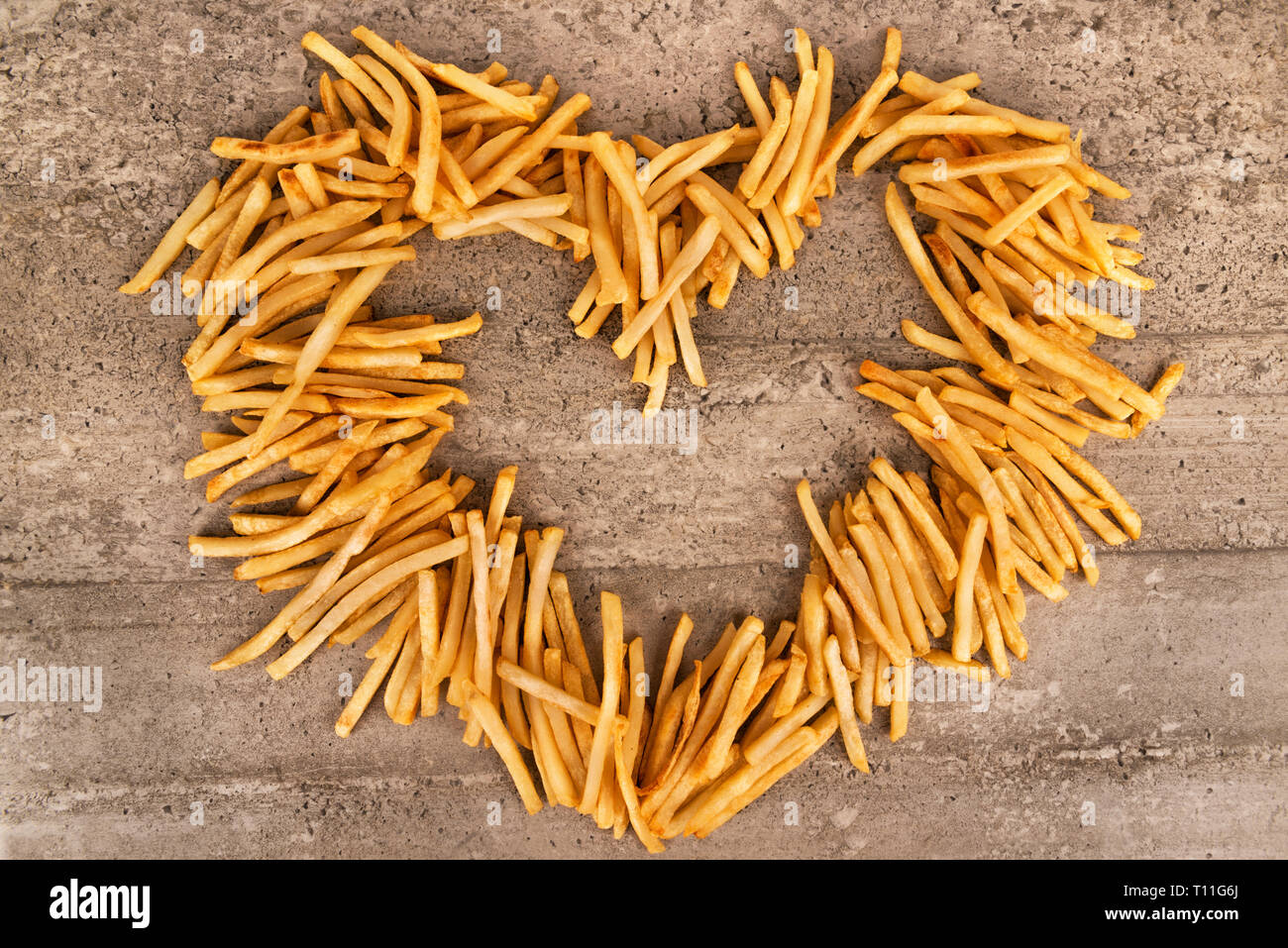 Forma di cuore di patate fritte isolato su sfondo concreto, direttamente al di sopra. Close up. Foto Stock