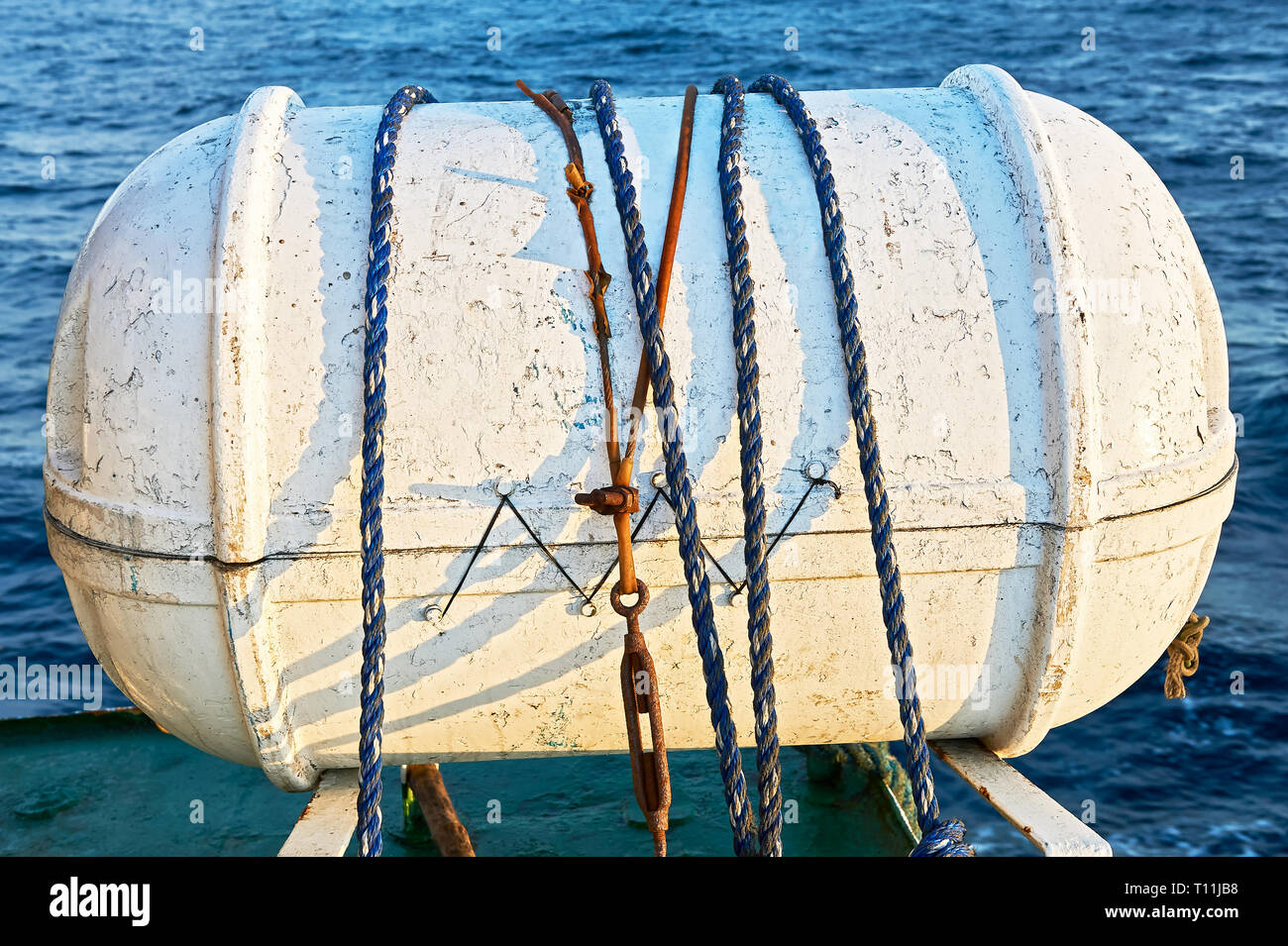 Close-up di un vecchio colorate di bianco zattera di salvataggio gonfiabile capsula detenute da corde sul ponte di un inter-isola nave in Asia Foto Stock