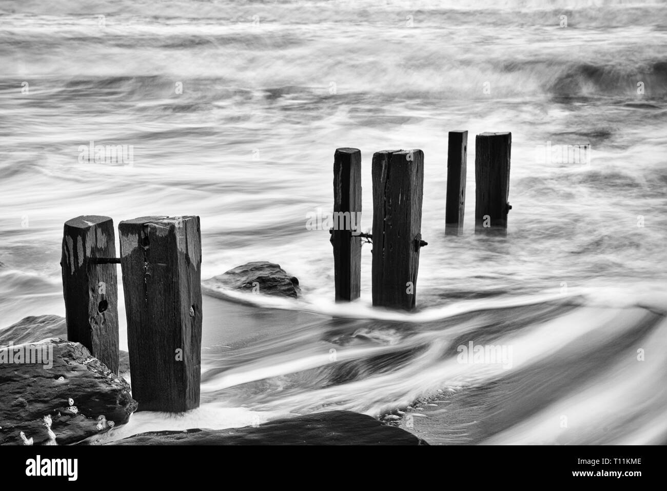 Una ruvida marea si rompe contro pennelli e rocce Foto Stock