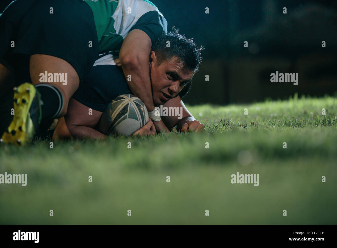 giocatore di rugby bloccato da giocatori di squadra opposti. gli uomini sportivi abbattono l'avversario durante la partita di rugby di notte. Foto Stock
