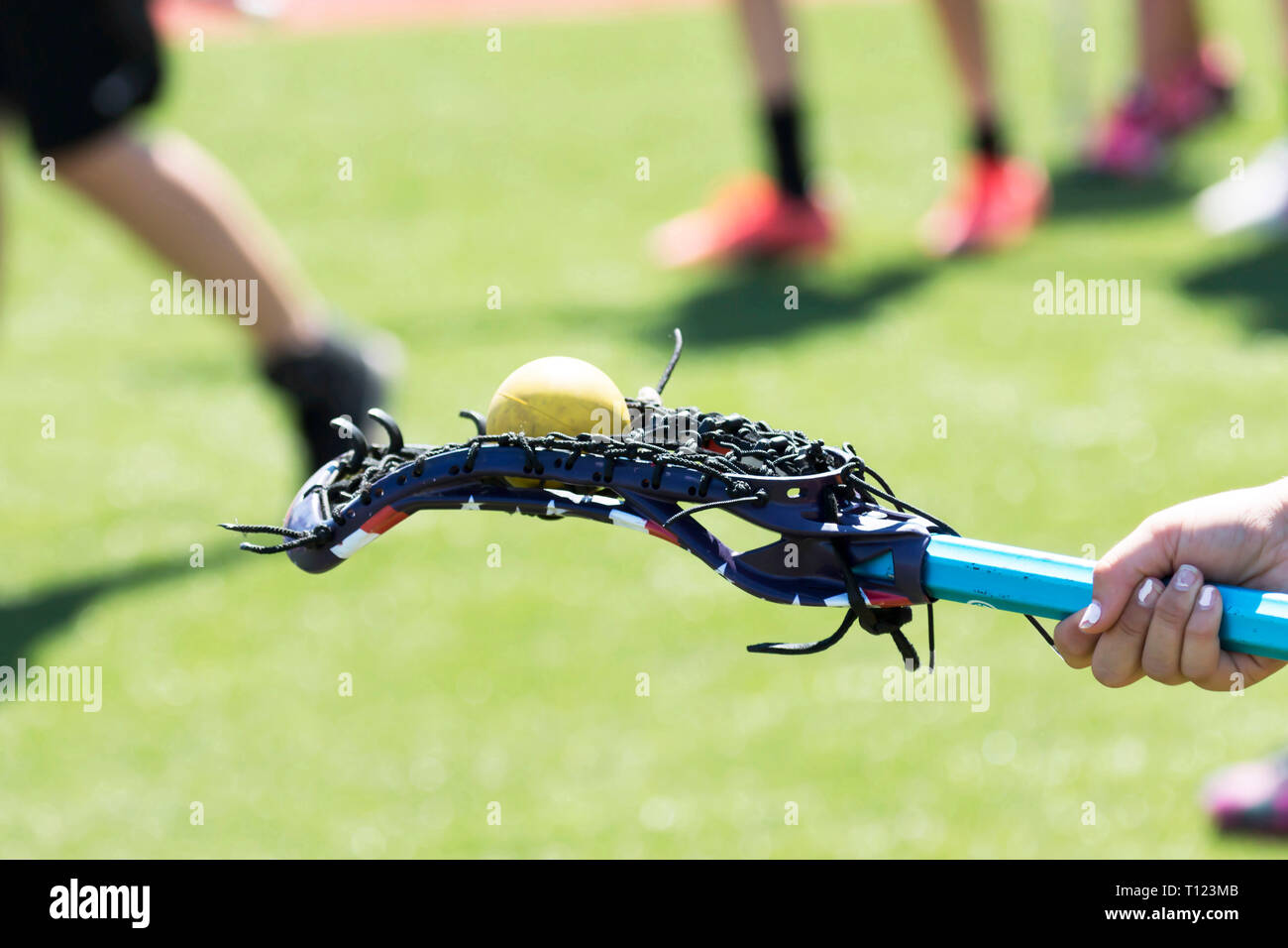 Una scuola di ragazze lacrosse atleta equilibra una sfera di colore giallo sul retro del suo bastone per divertimento. Foto Stock