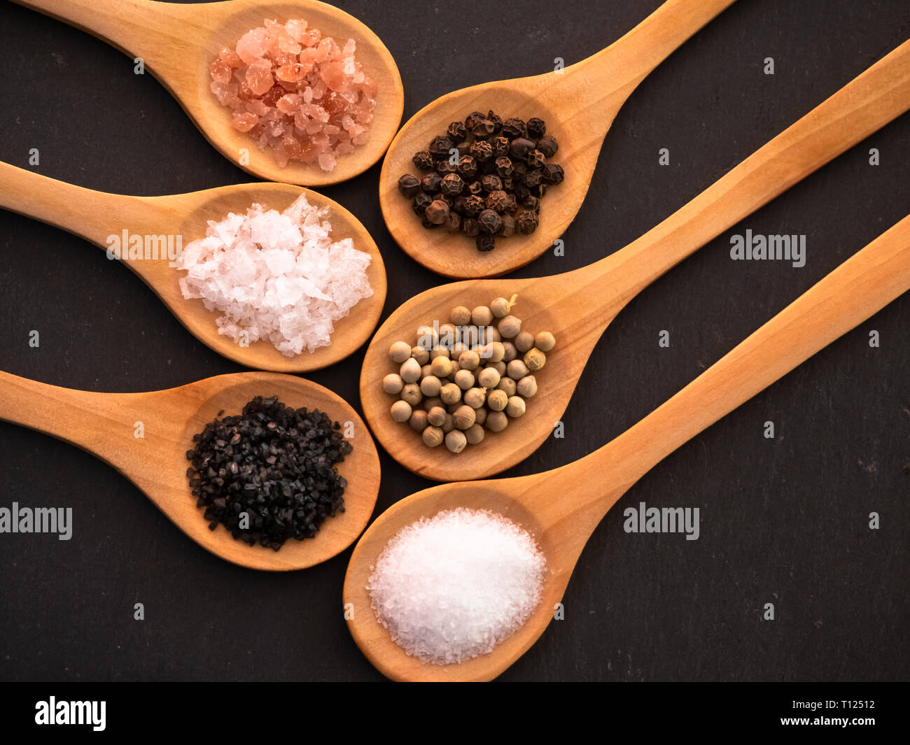 Cucchiai di legno con sale himalayano, nero hawaii sale, sale comune, fiocchi di sale e di pepe su una piastra di ardesia Foto Stock