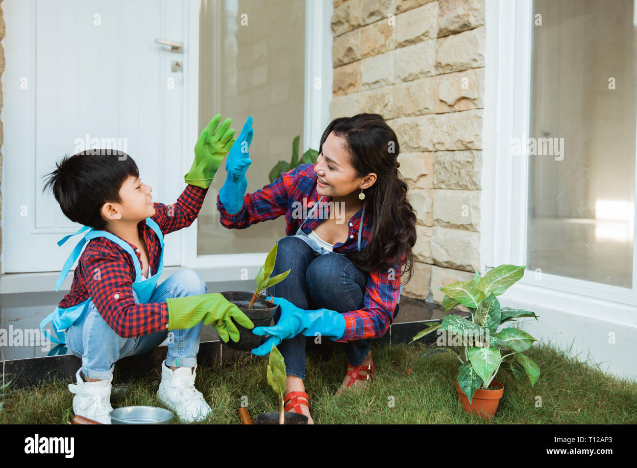 Madre e figlio highfive mentre il giardinaggio insieme a casa Foto Stock