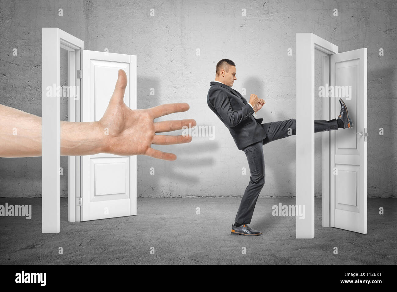 Imprenditore calci una porta ed una grossa mano che appaiono fuori da una porta aperta sul muro grigio sfondo Foto Stock