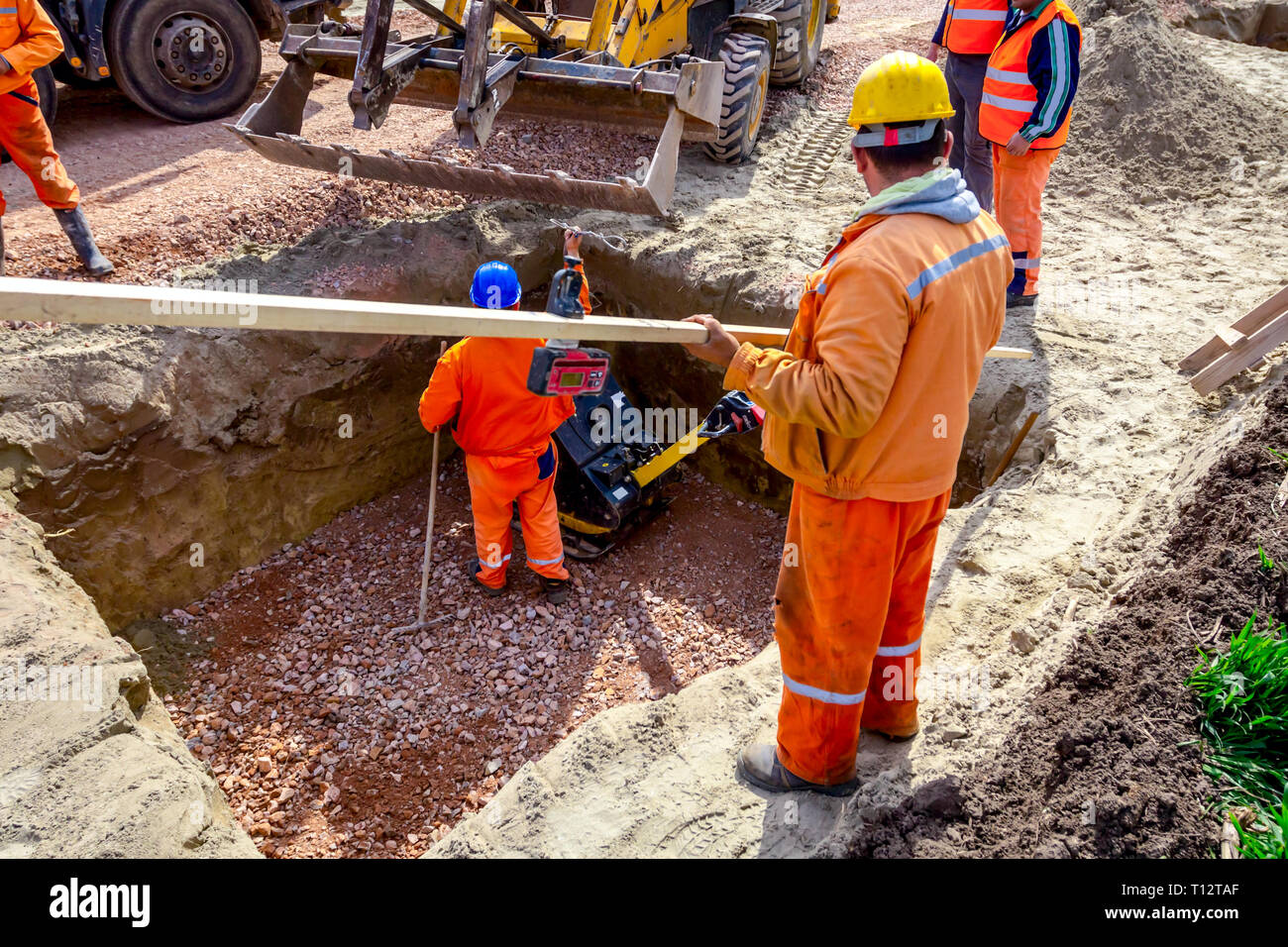 I lavoratori si stanno preparando per compattazione di ghiaia usando la piastra di vibrazione di macchina compattatore in trincea quadrata. Foto Stock