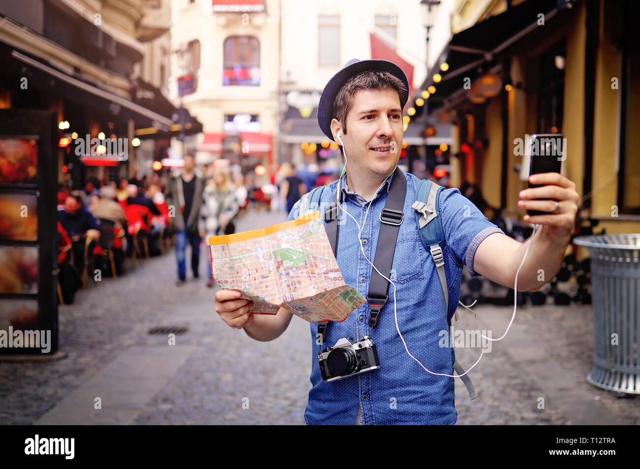 Giovane uomo turistico sulle strade della città vecchia, avente la mappa, vintage foto e fotocamera tenendo urbano selfie rottura con il suo smart phone fotocamera Foto Stock