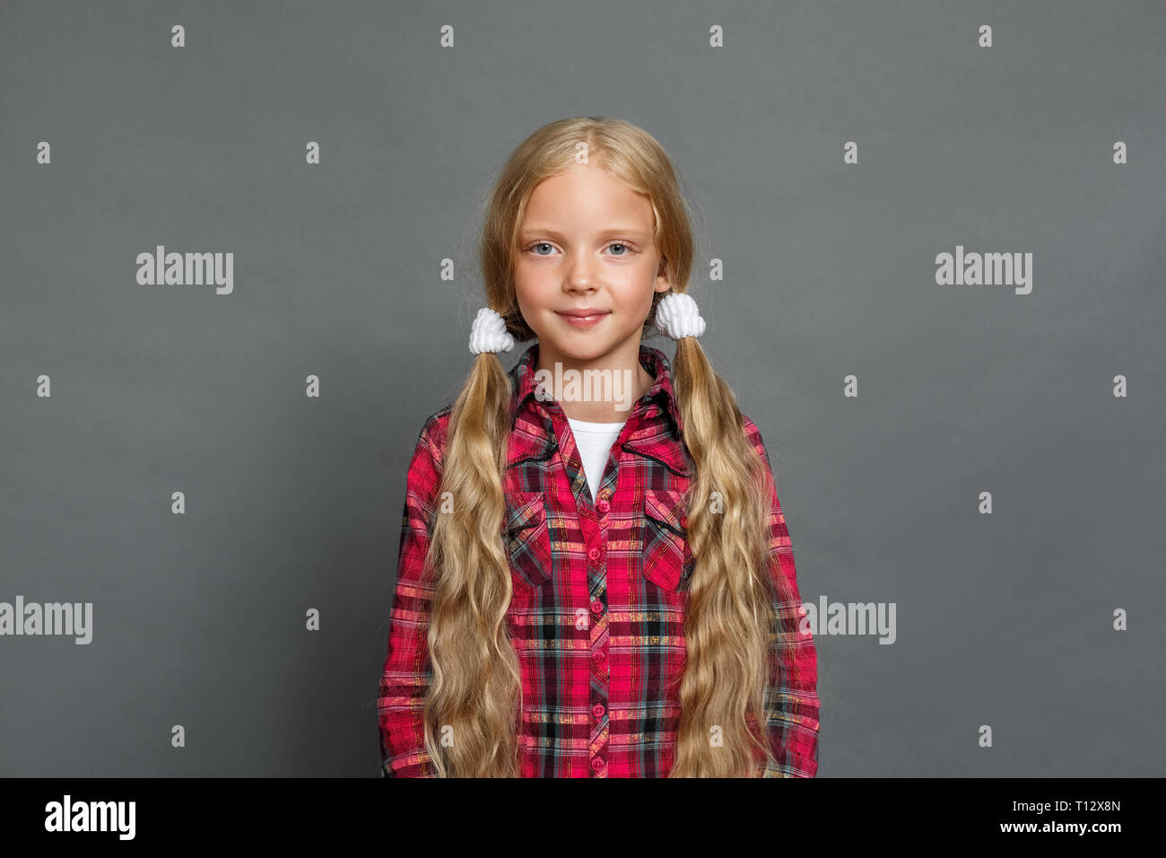 Bambina con due ponytails studio isolato in piedi sul muro grigio cercando fotocamera pacifica sorridente Foto Stock