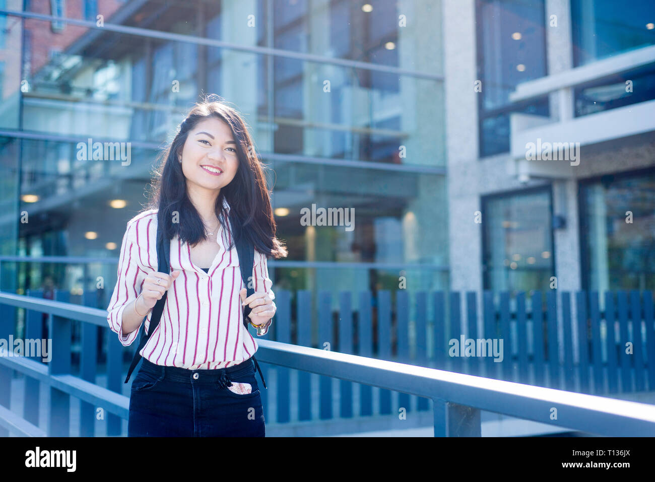 Una femmina di studenti asiatici in un moderno campus universitario in posa per una foto. Foto Stock