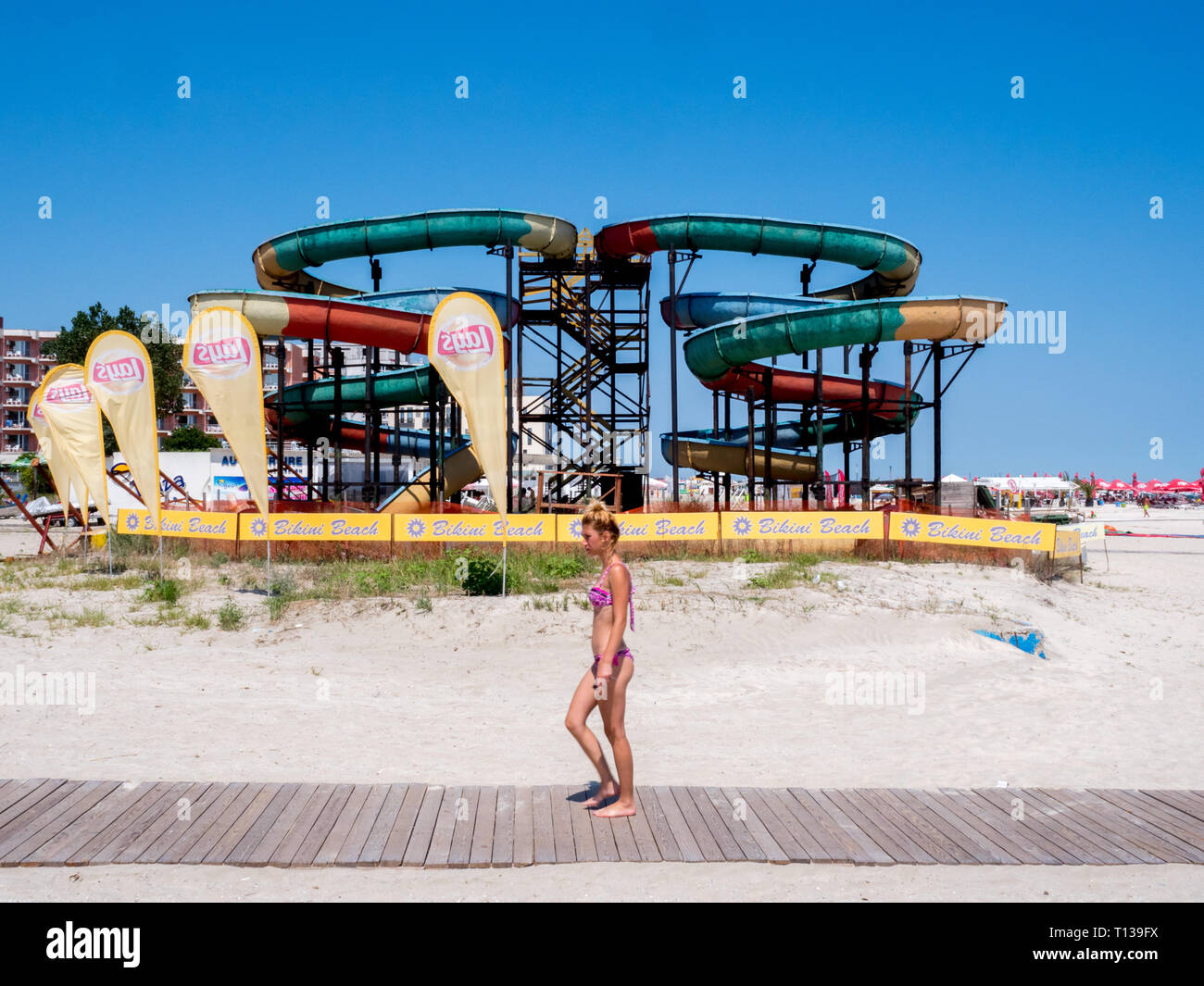 Una donna in un bikini rosa passeggiate da un acqua in disuso scorrere sulla spiaggia di Costanza. Foto Stock
