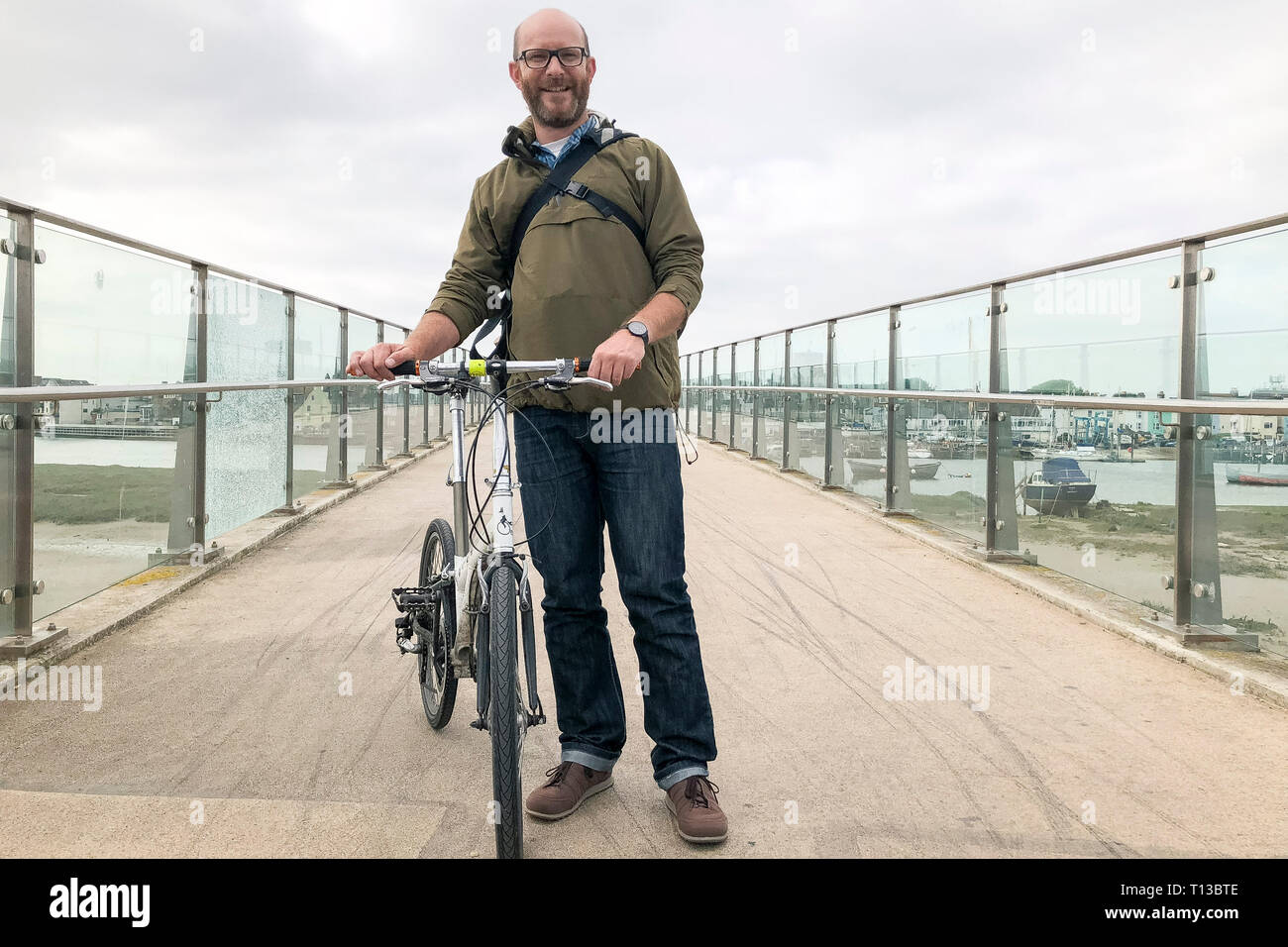 Un uomo bianco si erge su Shoreham Adur Ferry ponte con una bicicletta pieghevole Foto Stock