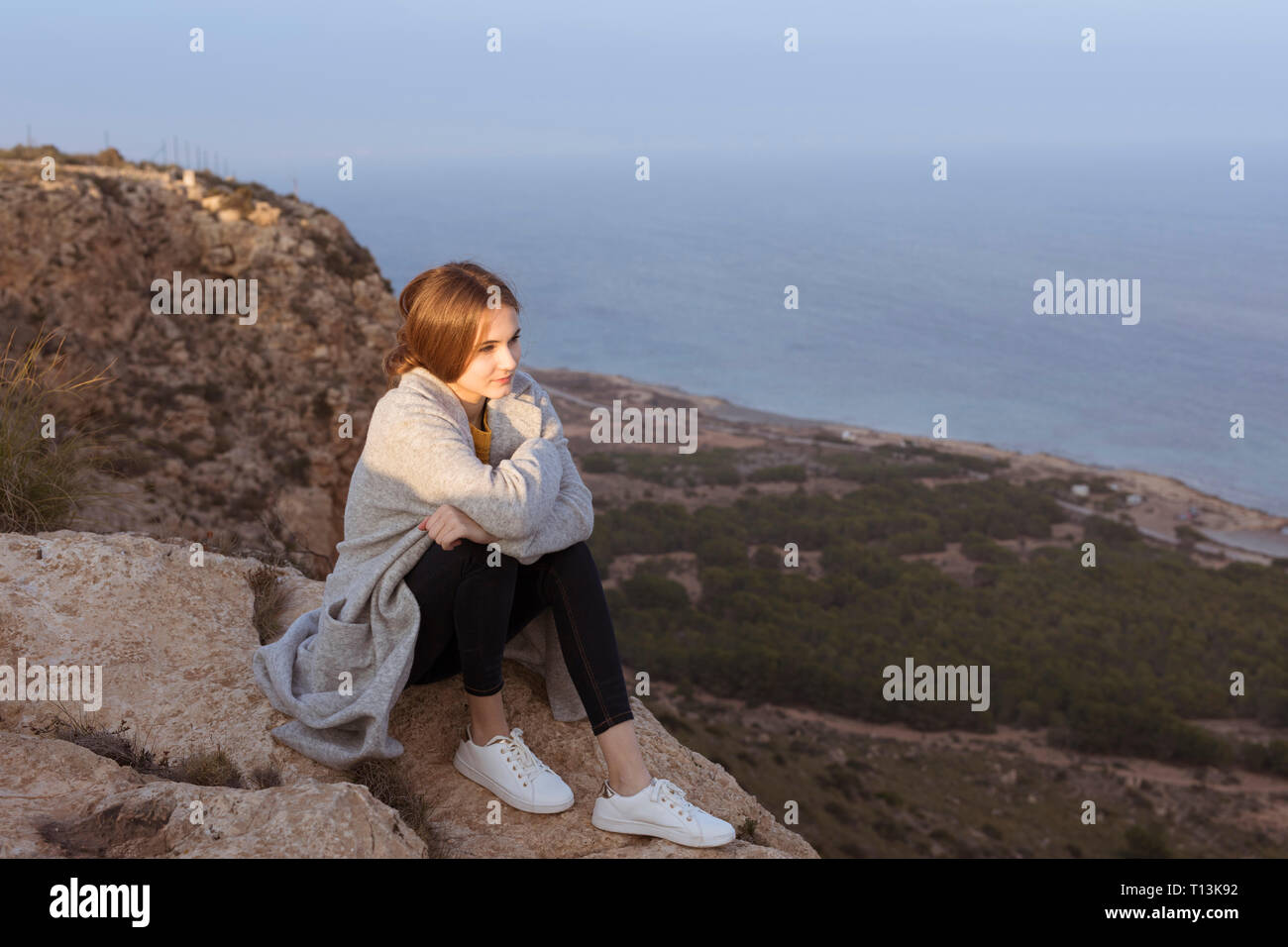 Spagna Alicante, Santa Pola, Cape Santa Pola, giovane donna seduta su roccia al tramonto Foto Stock