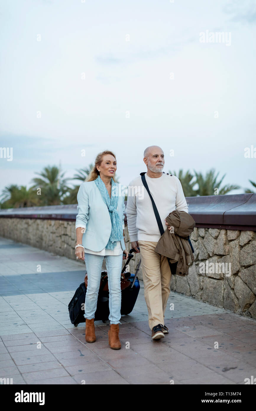 Spagna, Barcellona, coppia senior a piedi con i bagagli sul lungomare Foto Stock