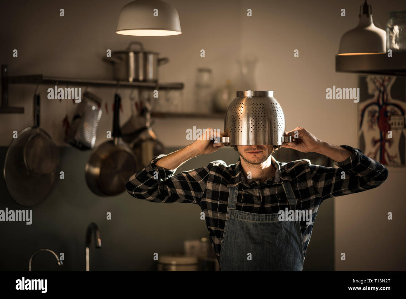 Uomo con grembiule in piedi in cucina, indossando scolapasta come casco Foto Stock