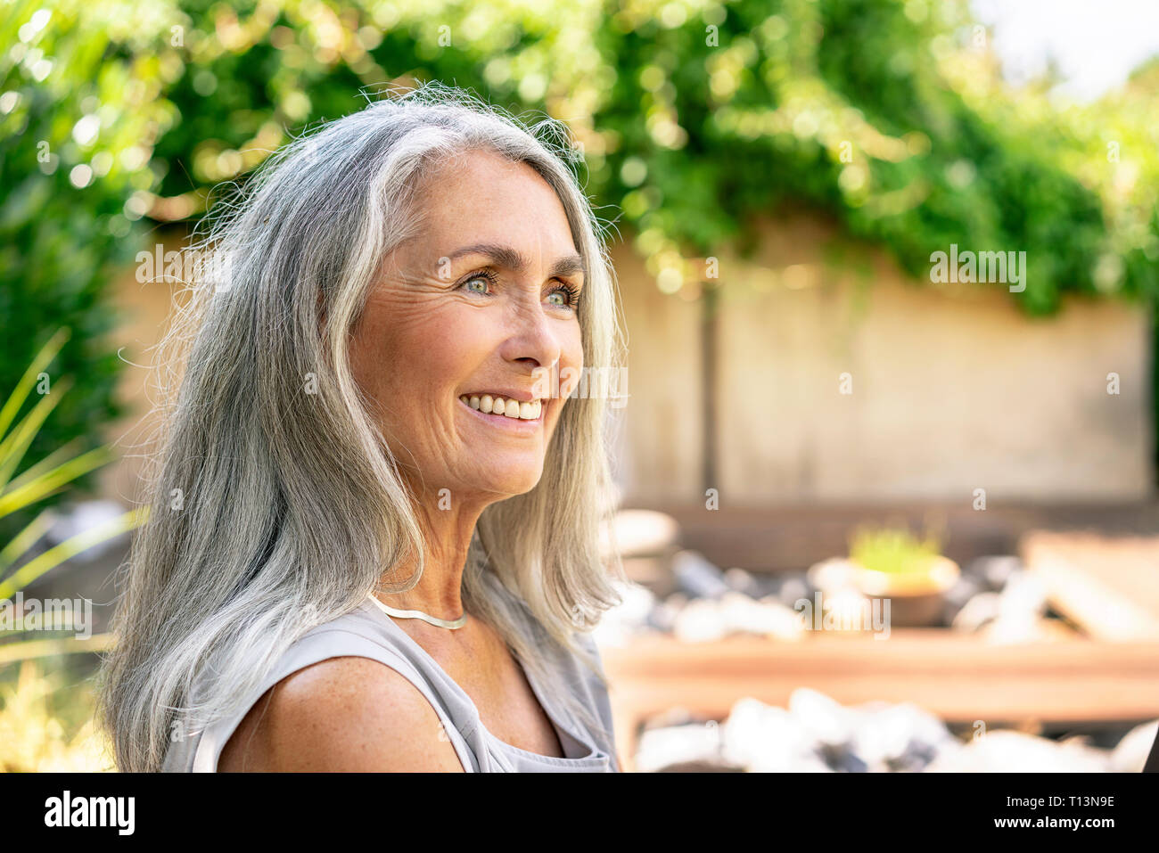 Ritratto di donna sorridente con lunghi capelli grigi in giardino Foto Stock