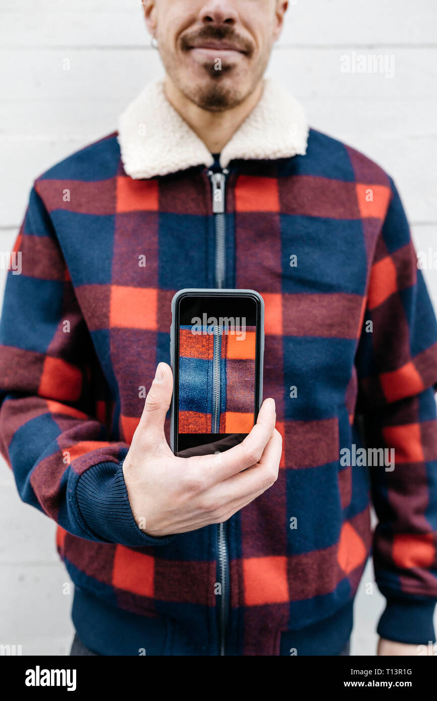 Giovane uomo che mostra una foto sul telefono con i colori della sua giacca Foto Stock