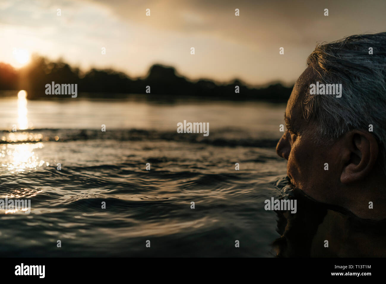 Senior uomo nuotare in un lago al tramonto Foto Stock