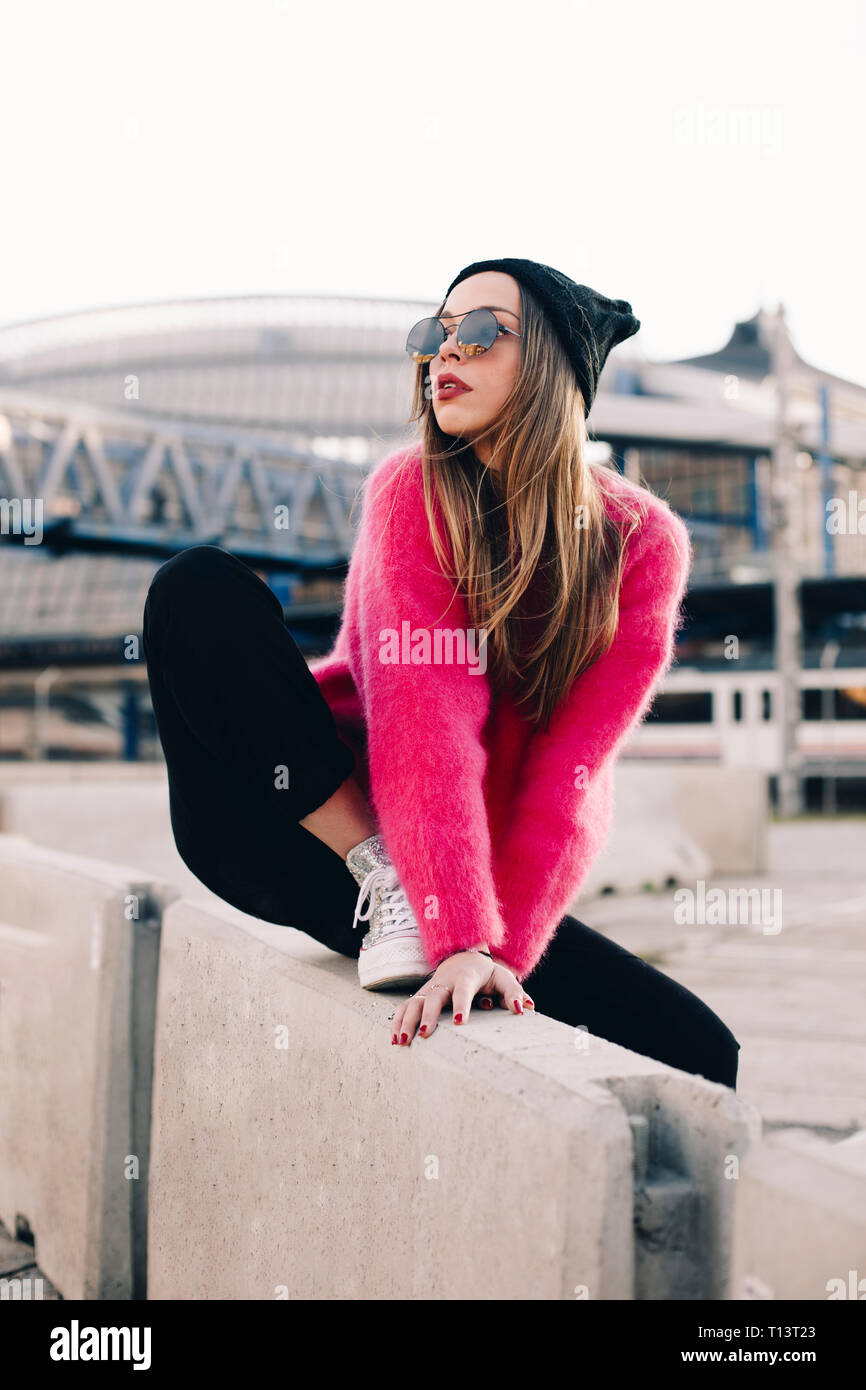 Ritratto di moda giovane donna che indossa gli occhiali da sole e cappello e rosa pullover a maglia Foto Stock