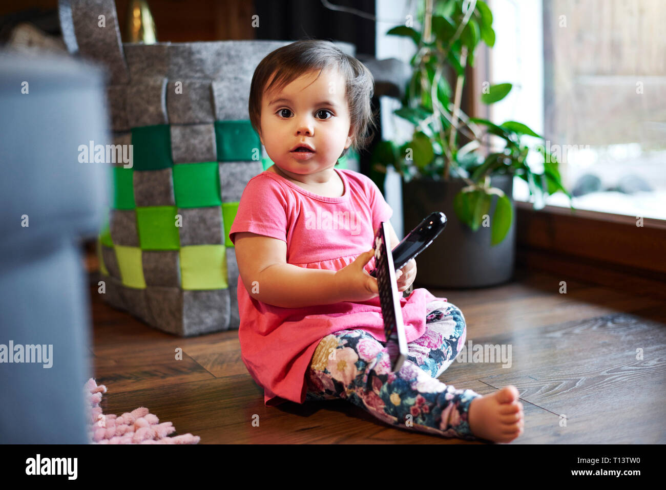 Ritratto di simpatici baby ragazza seduta sul pavimento a casa holding di controllo remoto Foto Stock