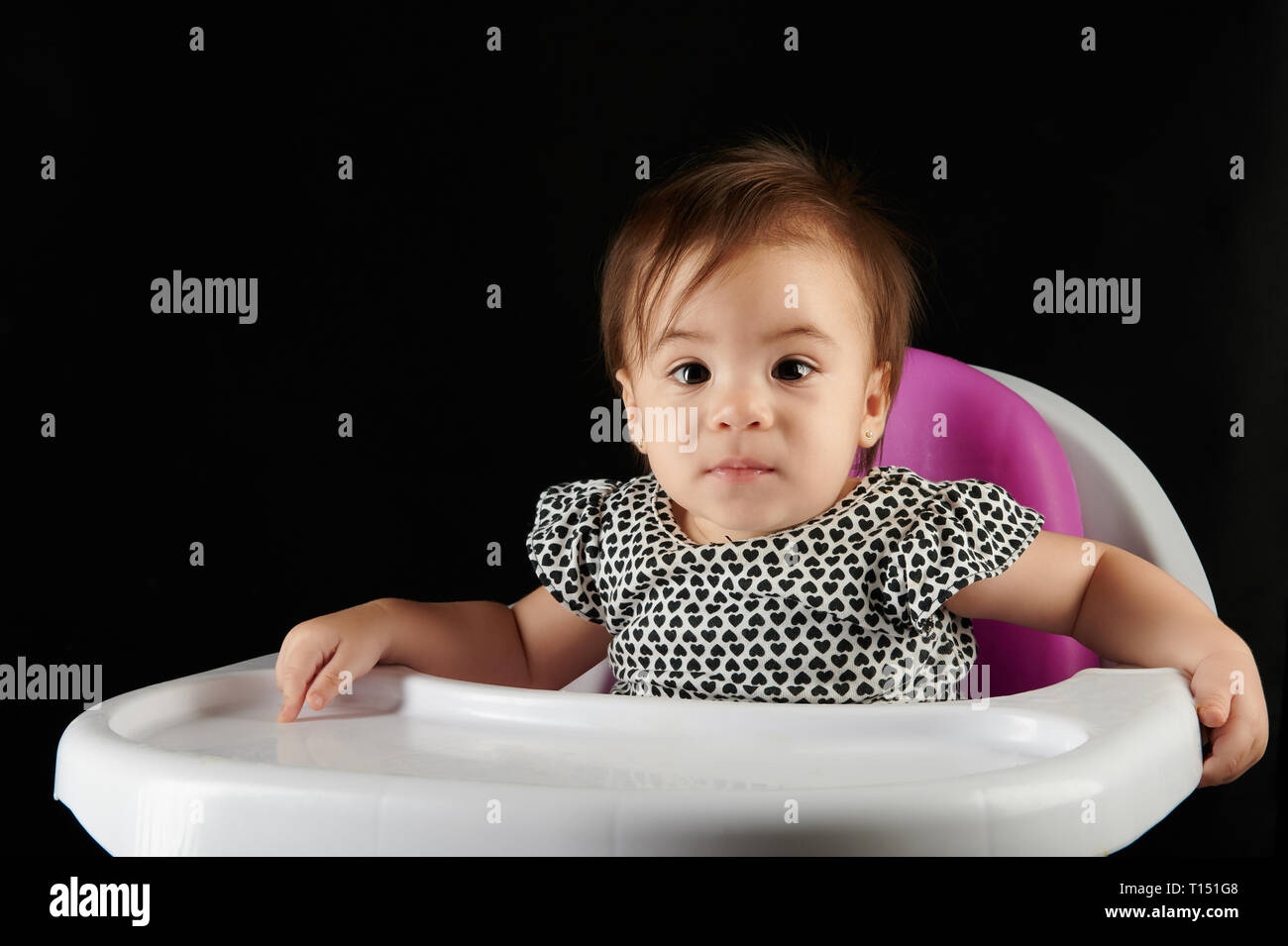 Baby girl sedere sulla sedia a mangiare tabella isolati su sfondo nero Foto Stock