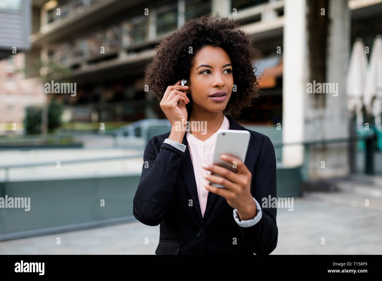 Ritratto di imprenditrice con lo smartphone a mettere su auricolari Foto Stock