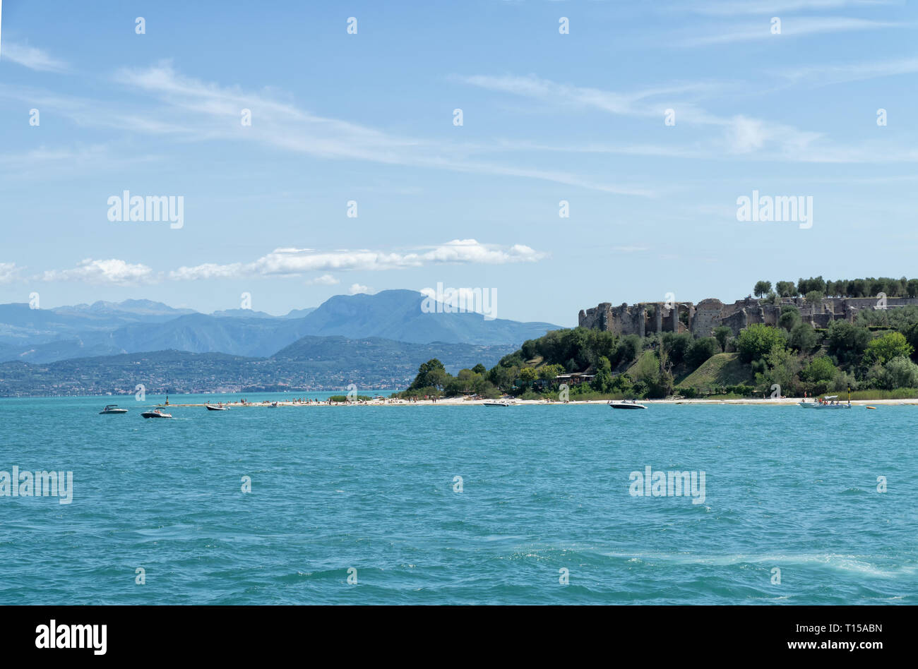 Spiaggia sassosa della cittadina di Sirmione sul Lago di Garda con vista delle Grotte di Catullo (Grotte di Catullo), le rovine di una villa romana costruita alla fine del 1 Foto Stock