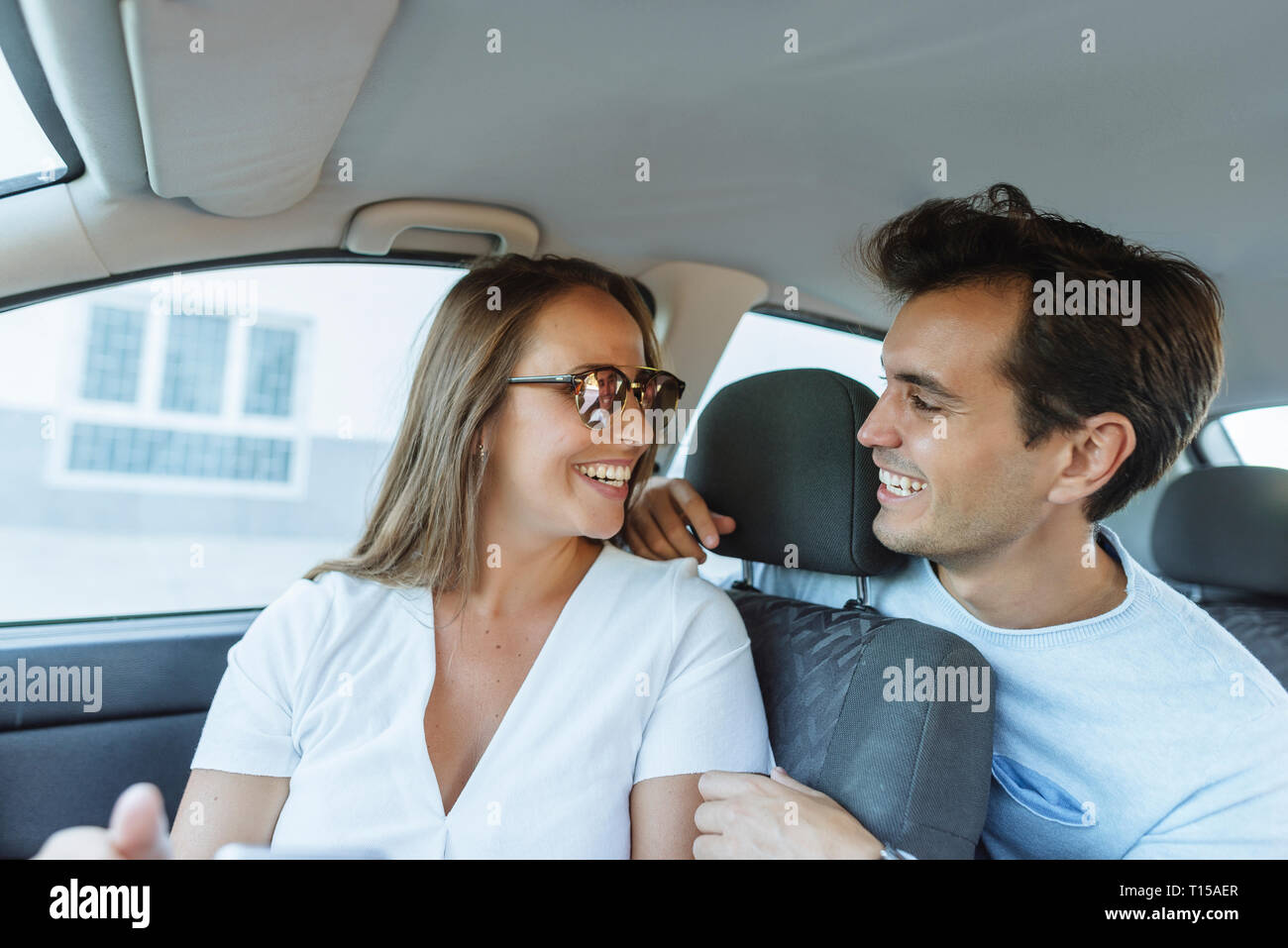 Coppia felice in auto con l'uomo sul sedile posteriore e la donna sul sedile passeggero anteriore Foto Stock