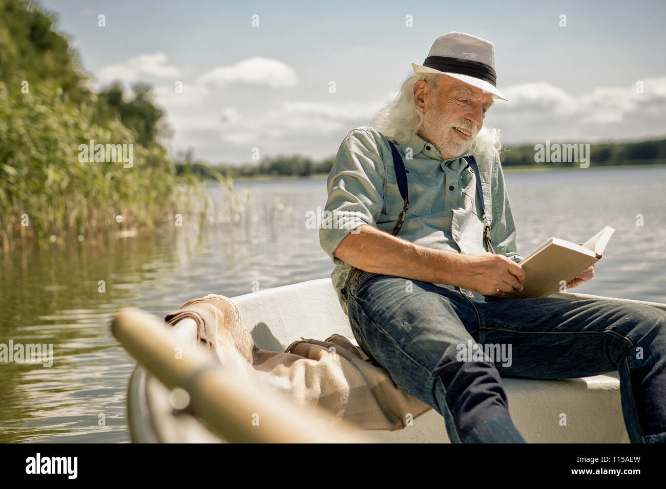 Ritratto di contenuto senior uomo seduto in barca a remi su un lago la lettura di un libro Foto Stock