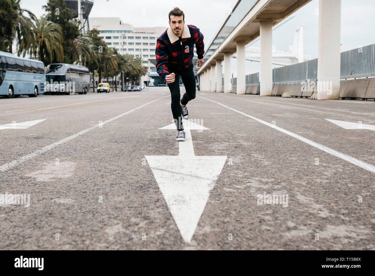 Giovane uomo con abiti casual appoggiata sul pavimento con un piede sulla parte superiore di una freccia dipinta sul pavimento Foto Stock