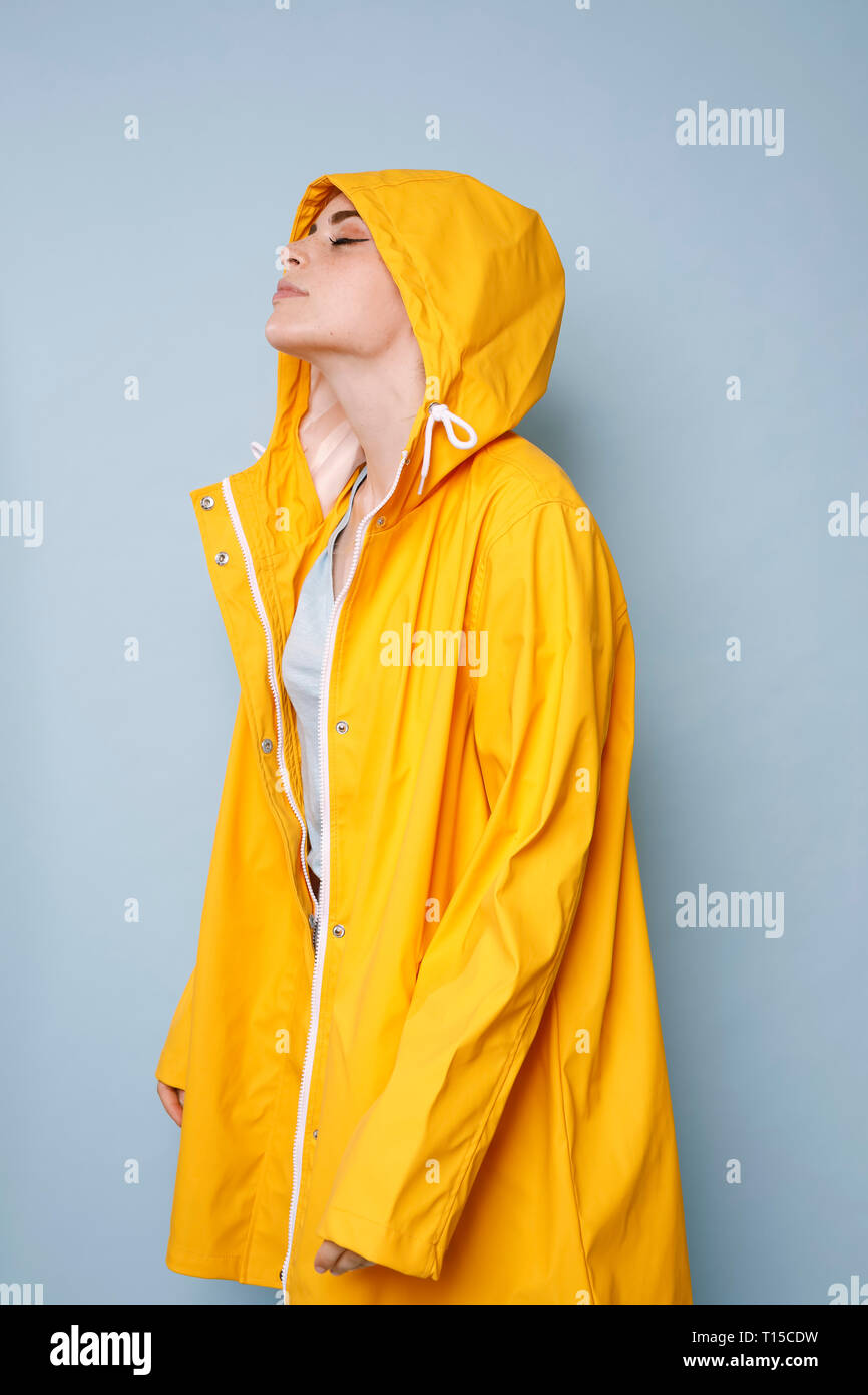 Giovane donna indossa giallo cappotto di pioggia di fronte a sfondo blu Foto Stock