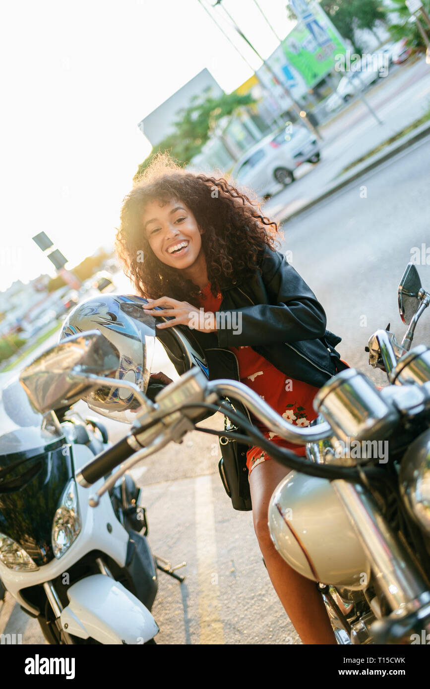 Ritratto di ridere giovane donna wsitting sul motociclo mettendo sul casco Foto Stock
