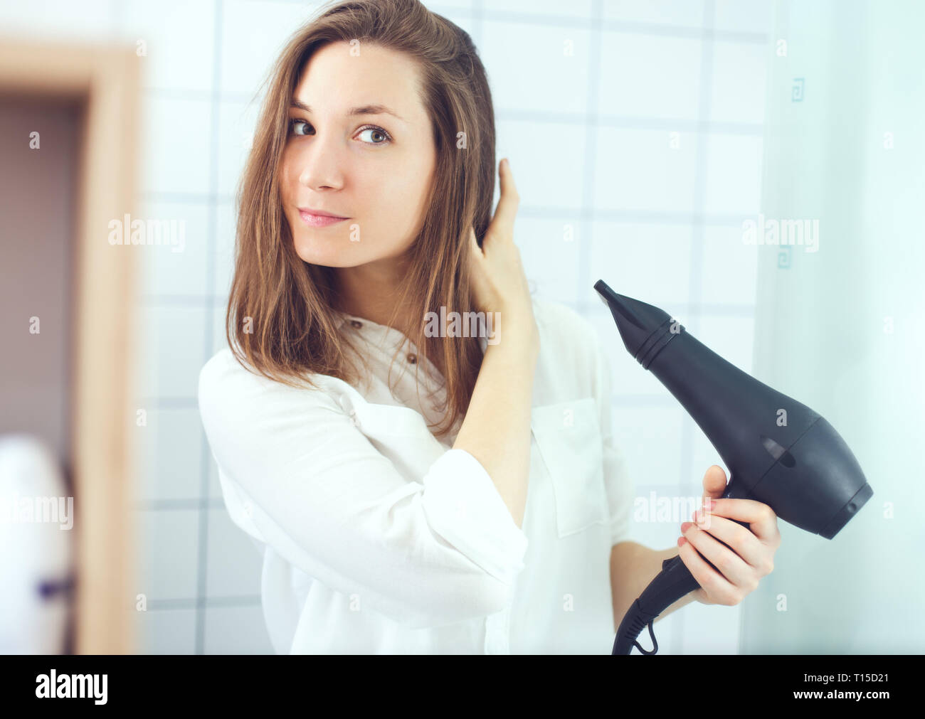 Bella giovane donna con phon asciugacapelli in bagno. Cura dei capelli Foto Stock