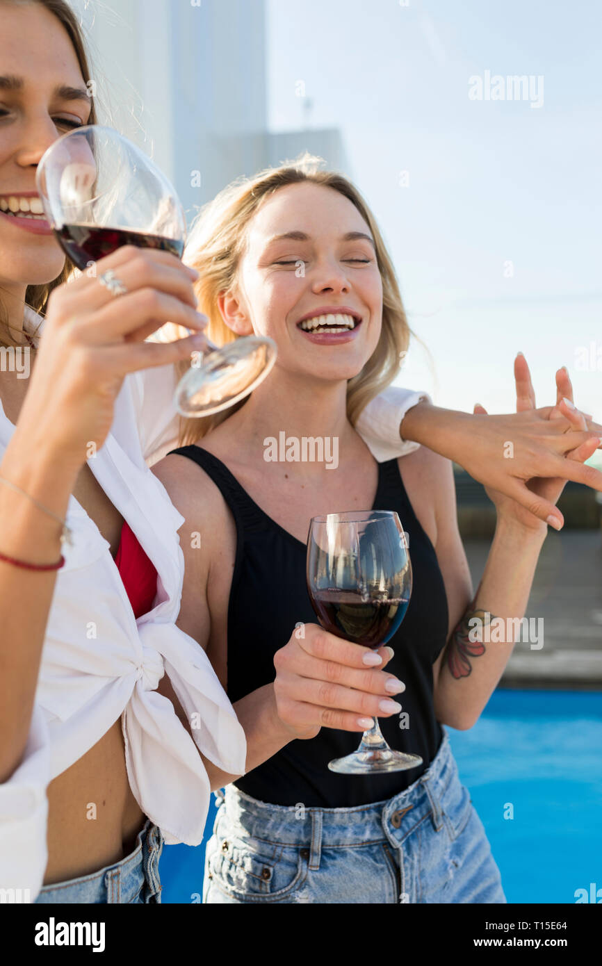 Amiche su di una terrazza sul tetto, divertirsi presso la piscina, bere vino rosso Foto Stock